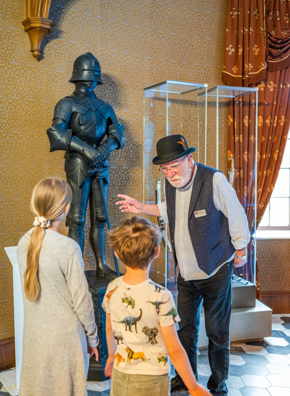 Kasteelgids legt de geheimen van het kasteel en de geschiedenis van het ridderharnas uit aan de kinderen // Ziet eruit als een harnas, maar is eigenlijk een oven: Mr Stohmann legt de geheimen van het kasteel uit. // © MV-T/Tiemann Kasteelgids legt de geheimen van het kasteel en de geschiedenis van het ridderharnas uit aan de kinderen