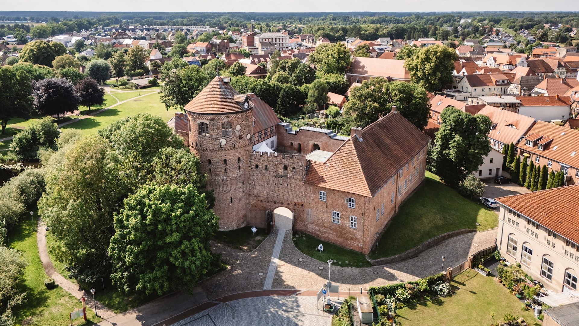 Een luchtfoto van het historische kasteel Neustadt-Glewe, omringd door groene bomen en de pittoreske oude stad met zijn rode pannendaken.