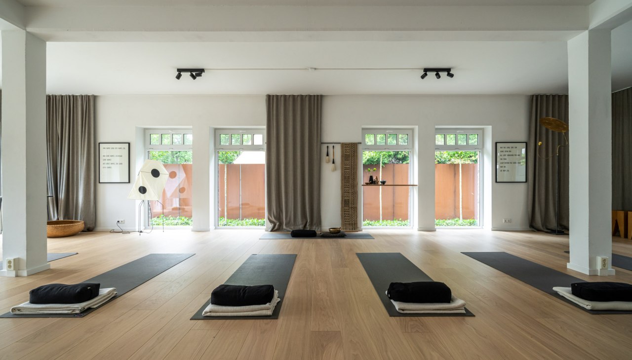 A modern, minimalist yoga and meditation room with light wooden floors, large windows and subtle decorations. The mats are already prepared for an upcoming yoga session, accompanied by soft cushions and towels., © Hotel Carpe Diem