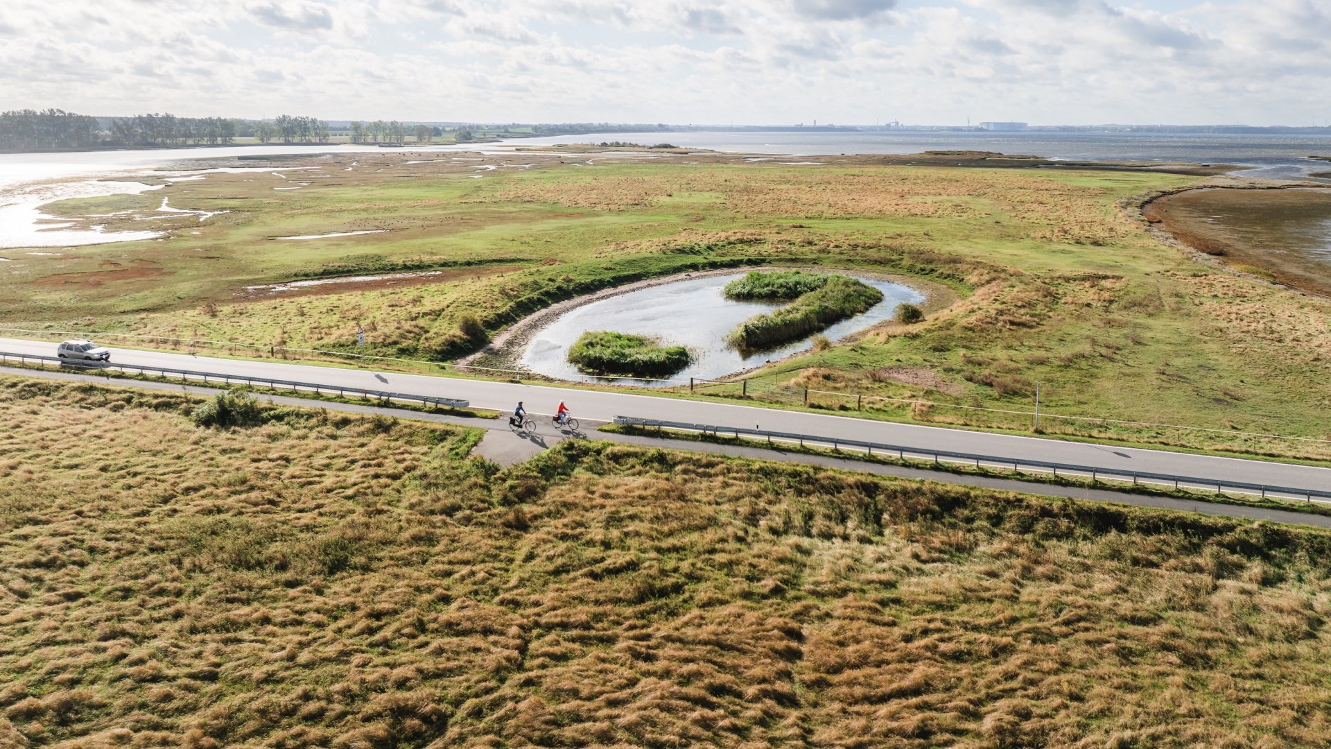  Aerial view of cyclists on a road leading through the green coastal landscape of the island of Poel.
