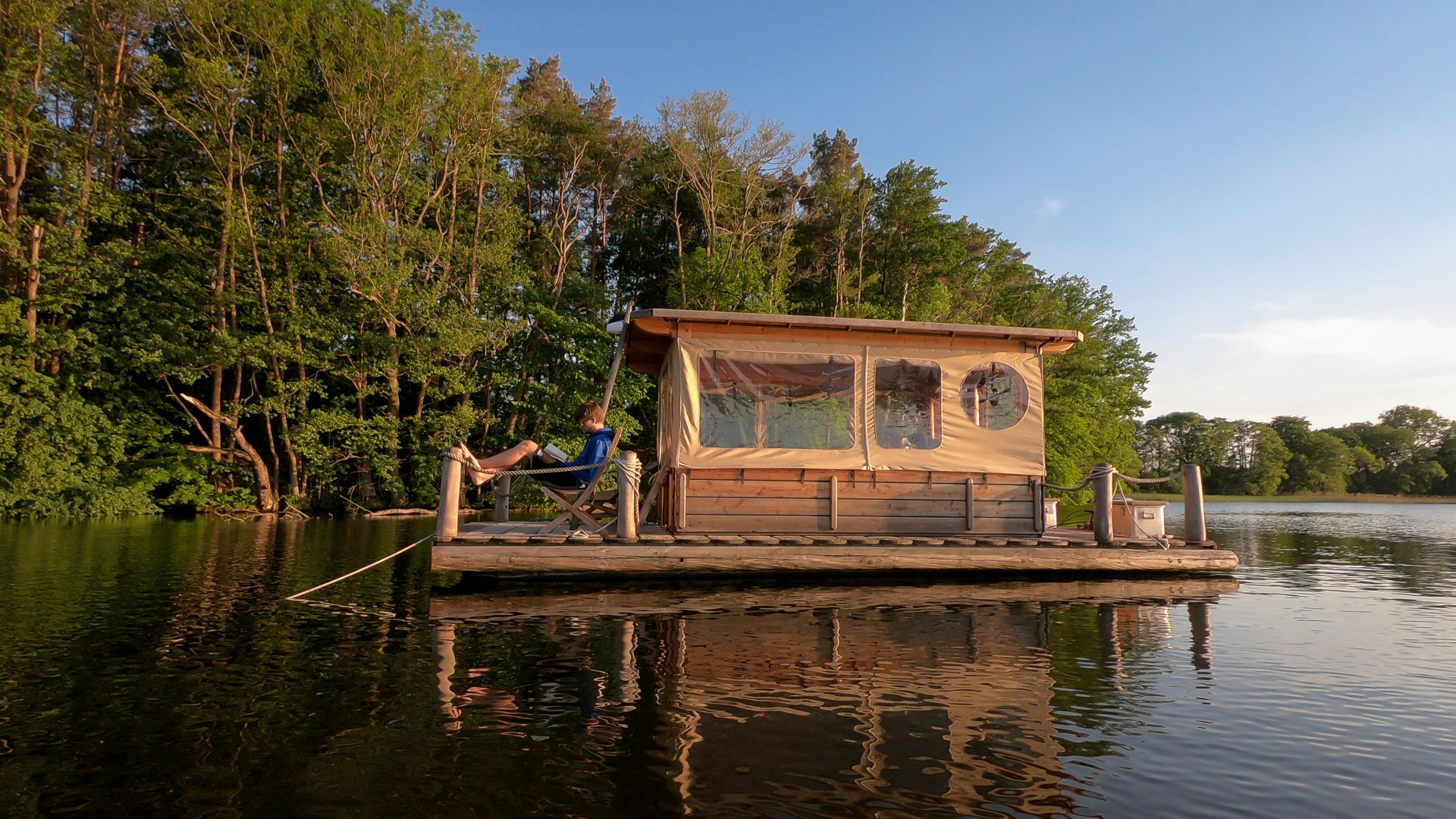 Een vlot glijdt rustig en dicht langs de oever over het water. Het is een zwem- en visbasis, zonnedek, natuurobservatiestation en vakantiehuis in &eacute;&eacute;n. En het mooie is dat er hier in het Mecklenburgse merengebied genoeg meren zijn voor iedereen om van een vergunningvrije raftvakantie te genieten. Dus gooi de trossen los! // &copy; MV-T/Myroad.de