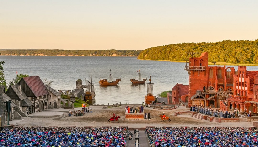 Podium van het Störtebeker Festival in Ralswiek op Rügen met publiek, middeleeuws decor en uitzicht op de Oostzee.