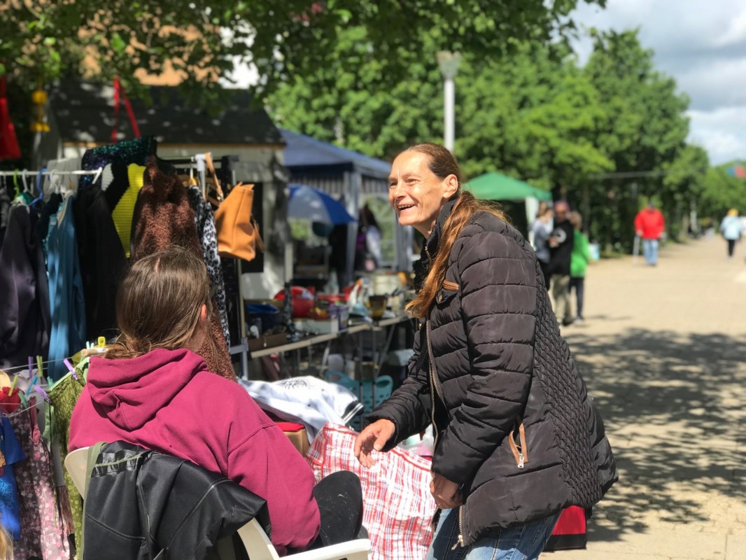 "Een moment vol ontmoetingen: tussen de kledingrekken, zonneschijn en kleine schatten gaat het op onze rommelmarkt niet alleen om kopen en verkopen - het gaat om kletsen, lachen en genieten van elkaars gezelschap.", &copy; LGE-MV