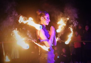 Beim Lampionfest im Zoo Rostock f&uuml;hrt eine Frau mit Gesichtsschminke eine Feuershow vor und h&auml;lt einen brennenden Stab in der Hand. // &copy; Zoo Rostock/ Kloock