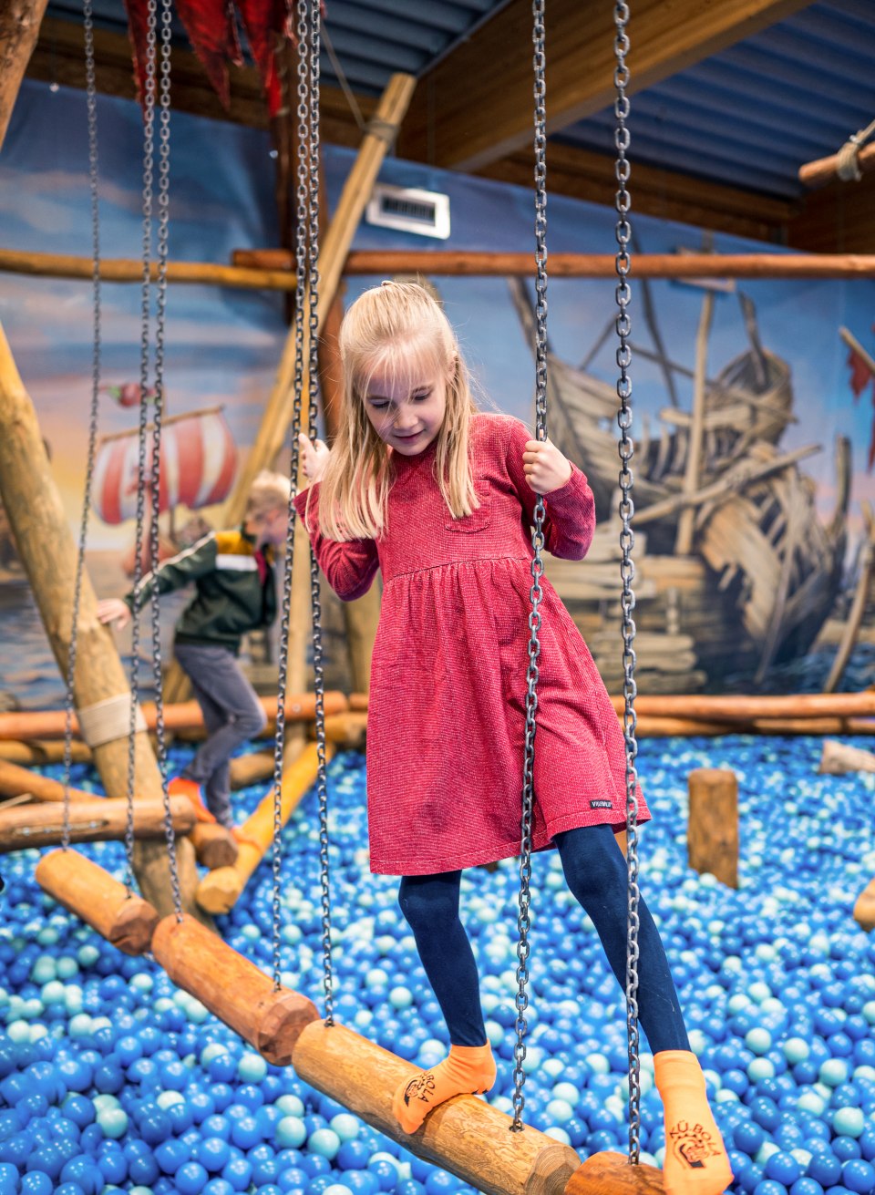 A child balances over a ball pool in the indoor playground.