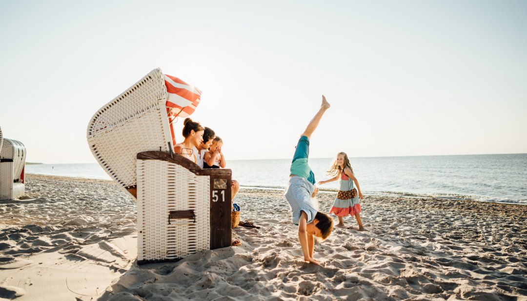 Familie op het Oostzeestrand in Dierhagen met een strandstoel, kinderen doen handstanden en spelen in het zand.