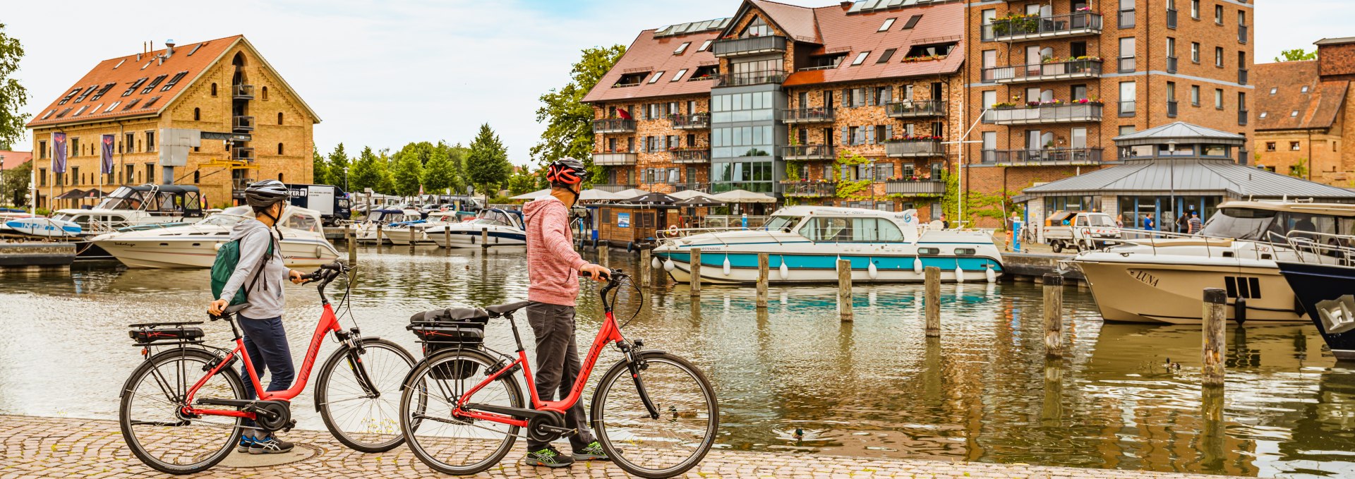 De haven van de koninklijke zetel van Neustrelitz - waar een echtpaar met fietsen staat. // Fietsers en boottoeristen ontmoeten elkaar hier, in de haven van de koninklijke zetel van Neustrelitz // © MV-T/Tiemann De haven van de koninklijke zetel van Neustrelitz - waar een echtpaar met fietsen staat.