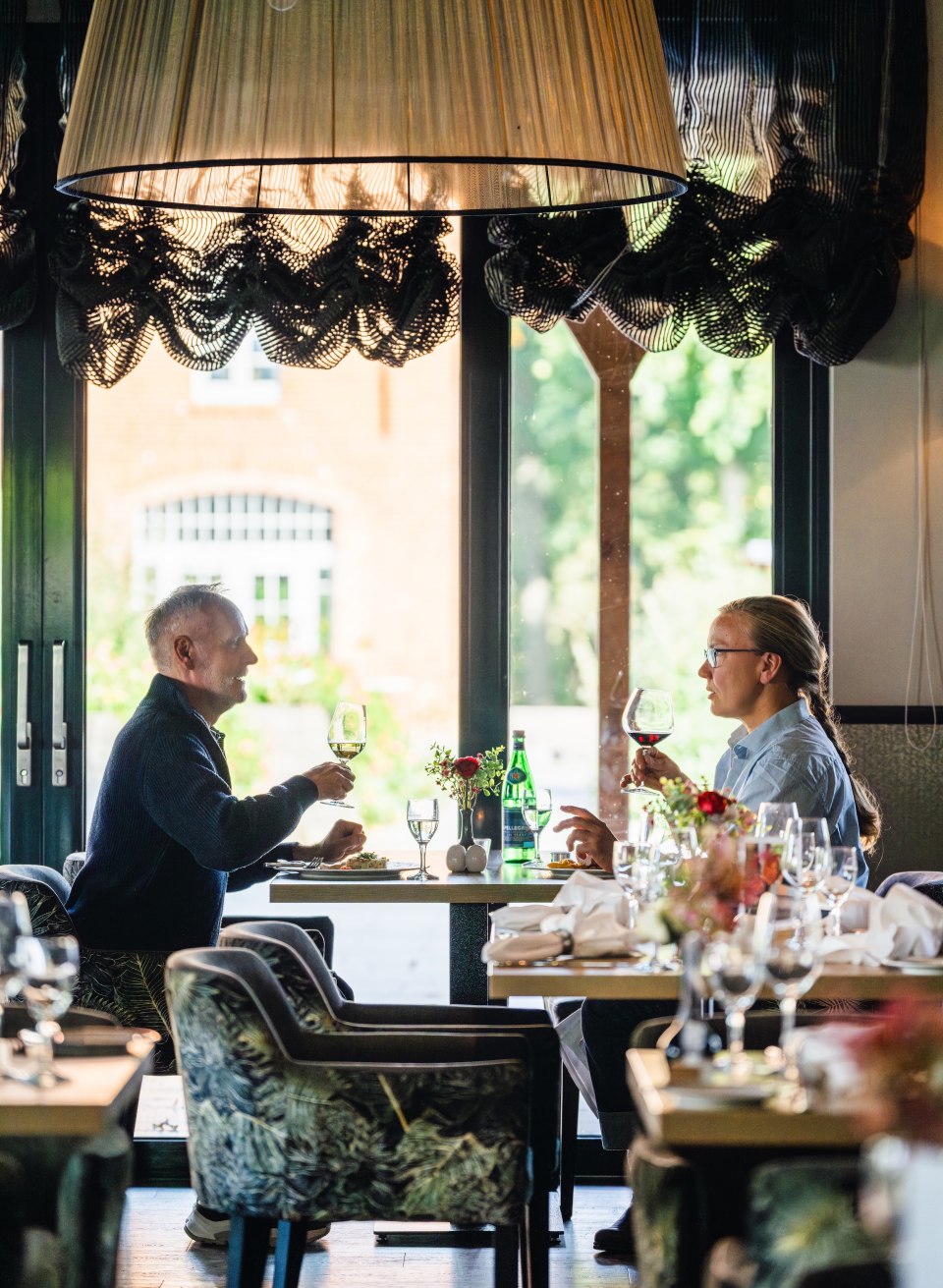 Twee mensen proosten met een glas wijn terwijl ze genieten van een elegante lunch in het restaurant van Schloss Basthorst.