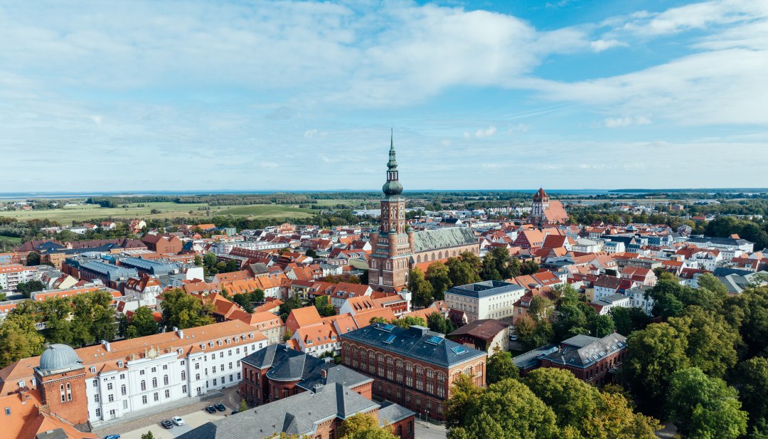 The silhouette of Greifswald from the air and view of the church towers and old town by day.