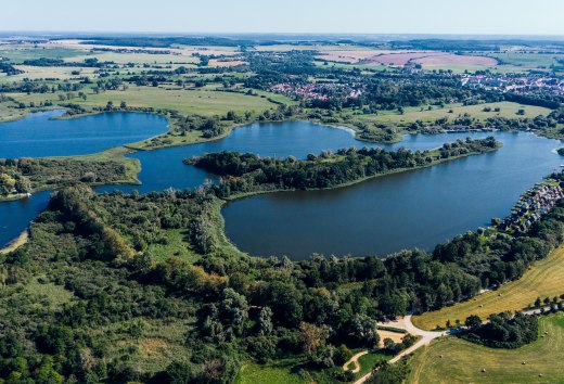 Aerial view of Lake Teterow with Burgwallinsel, green shores, fields and Teterow in the background. // Wide expanses of water and green shorelines frame the Burgwallinsel in Lake Teterow - space to take a deep breath and explore in Mecklenburg-Vorpommern. // © MV-T/Gänsicke Aerial view of Lake Teterow with Burgwallinsel, green shores, fields and Teterow in the background.