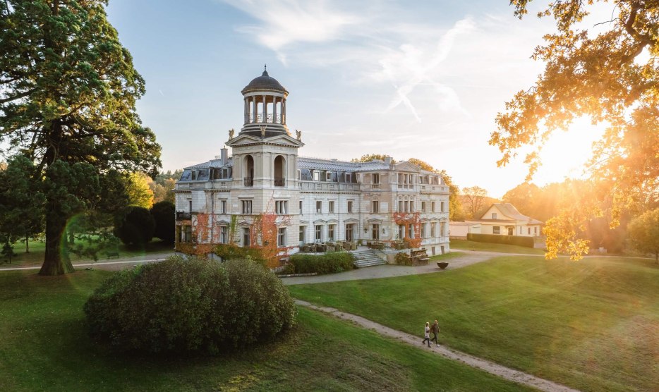 Kaarz Castle in Mecklenburg-Schwerin at sunset with walkers in the well-tended castle park.