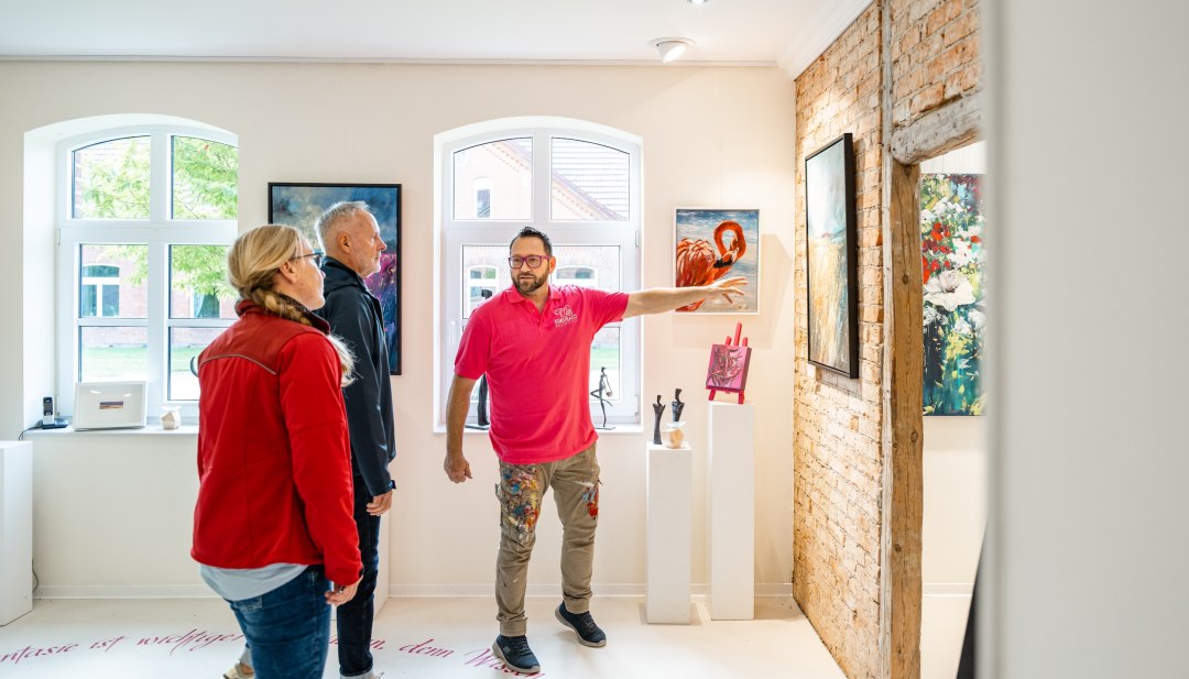 Art tour in a bright gallery with visitors in front of paintings and exposed wooden beams in Basthorst.