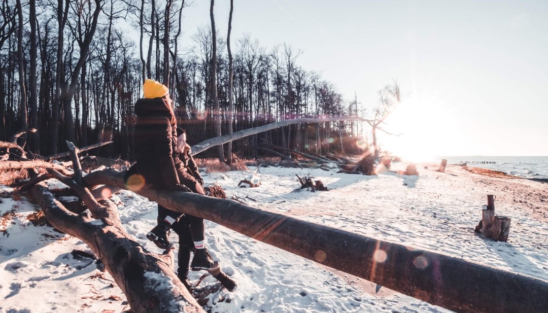 Dompel je onder in het rustige winterlandschap langs de besneeuwde Baltische kust bij Torfbrücke en voel de kracht van de natuur., © TMV/Scholz-Winter Twee mensen in winterkleding wandelen op een besneeuwd Oostzeestrand bij Torfbrücke bij zonsondergang.