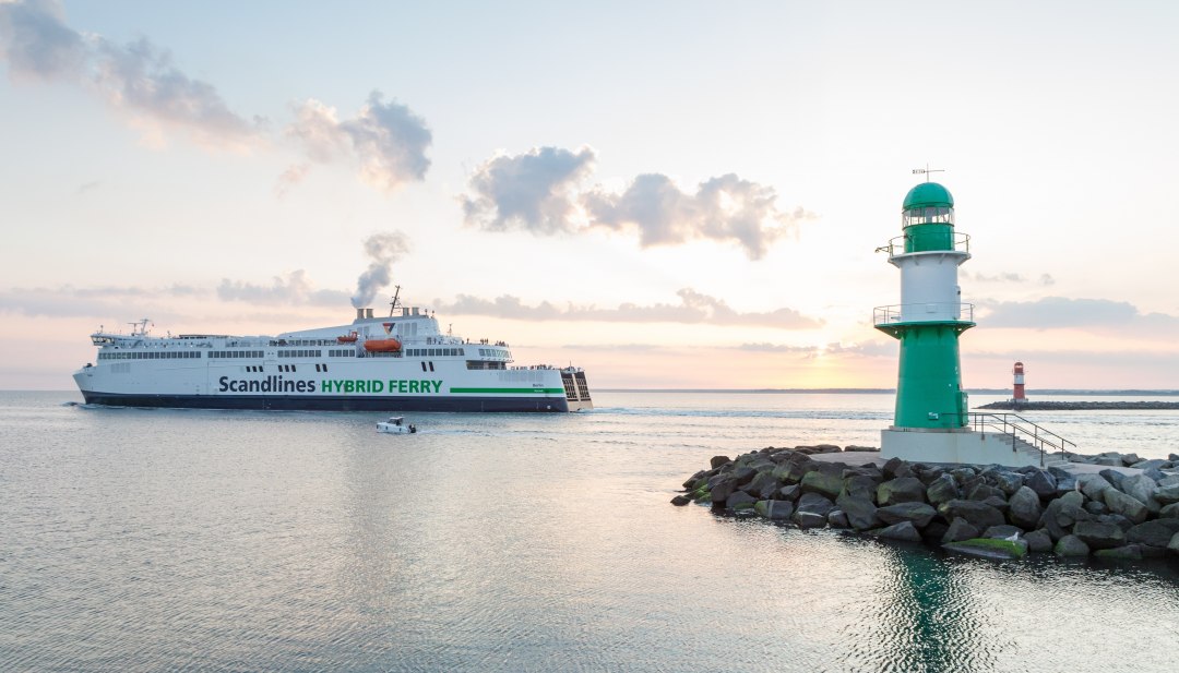 Scandlines hybrid ferry passes the lighthouses in Warnemünde harbor at sunset.