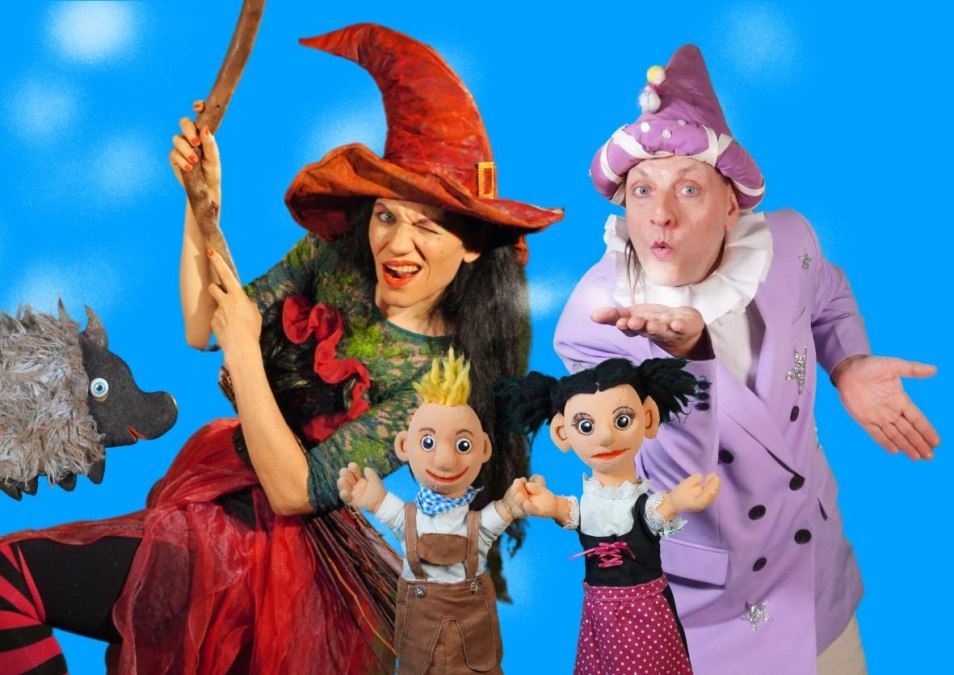 Two puppeteers dressed as a witch and a wizard and two hand puppets Hansel and Gretel in front of a blue background, © Theater Phoebus