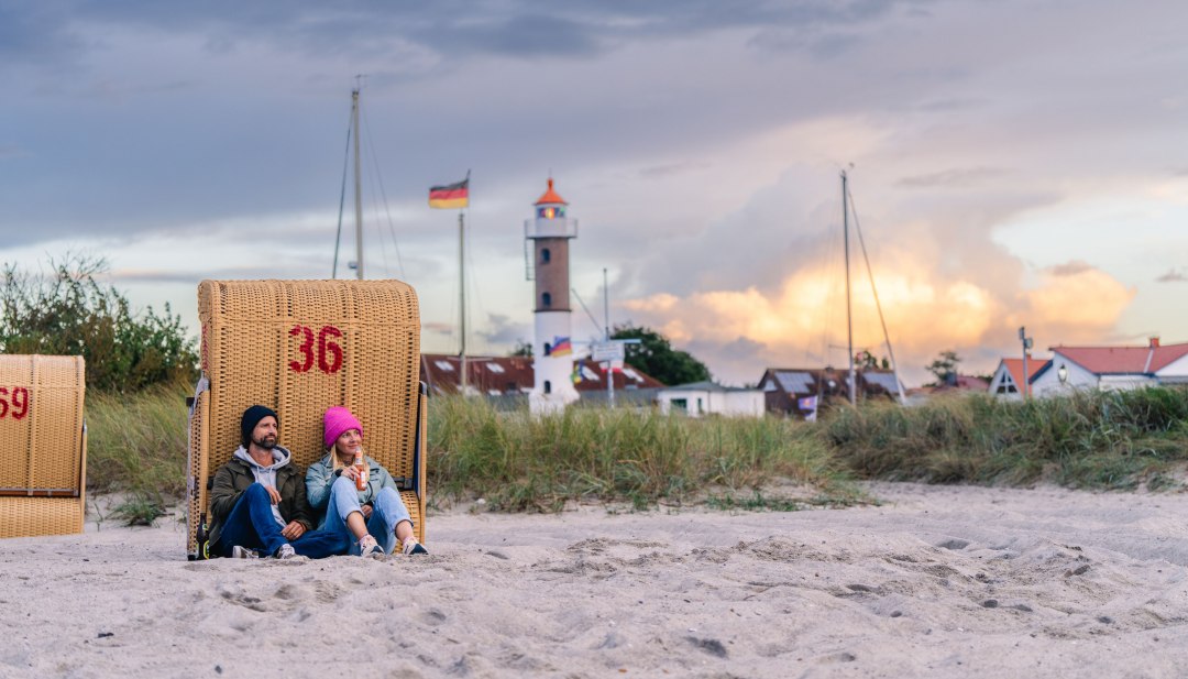Couple sitting in a beach chair on the beach in Timmendorf on Poel with a view of the lighthouse and the evening sky.