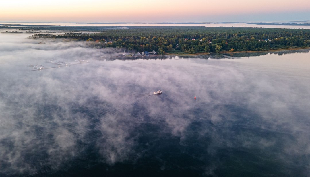 Luchtfoto van de Müritz in de vroege ochtend met mistflarden waar een boot langzaam doorheen vaart.