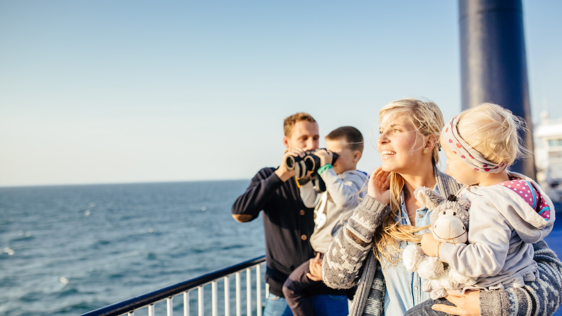 Family with children stand on the deck of a ferry and look out over the Baltic Sea in sunny weather.