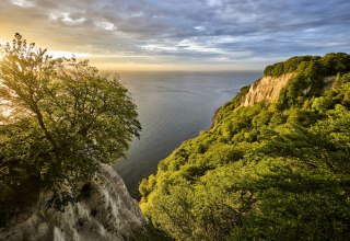 From the Skywalk K&ouml;nigsstuhl near Sassnitz, the view sweeps over glowing chalk cliffs and the vast Baltic Sea. Beech forest frames the bright cliffs while the light breaks through dramatic clouds - a natural spectacle on R&uuml;gen that will remain in your memory. // &copy; Florian Trykowski