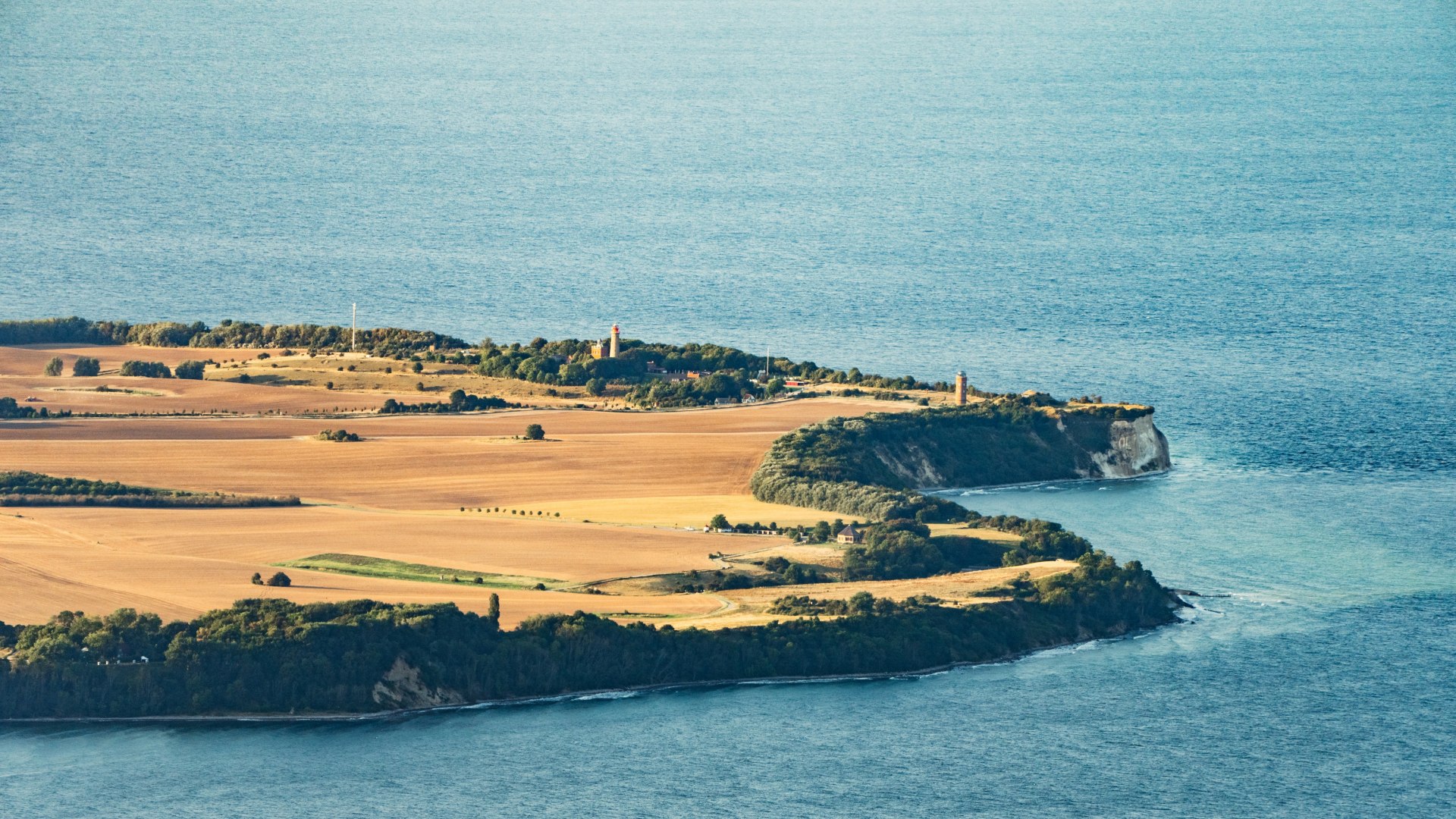 Aerial view of Cape Arkona on the island of Rügen, showing lighthouses and wide fields surrounded by the deep blue sea of the Baltic Sea.