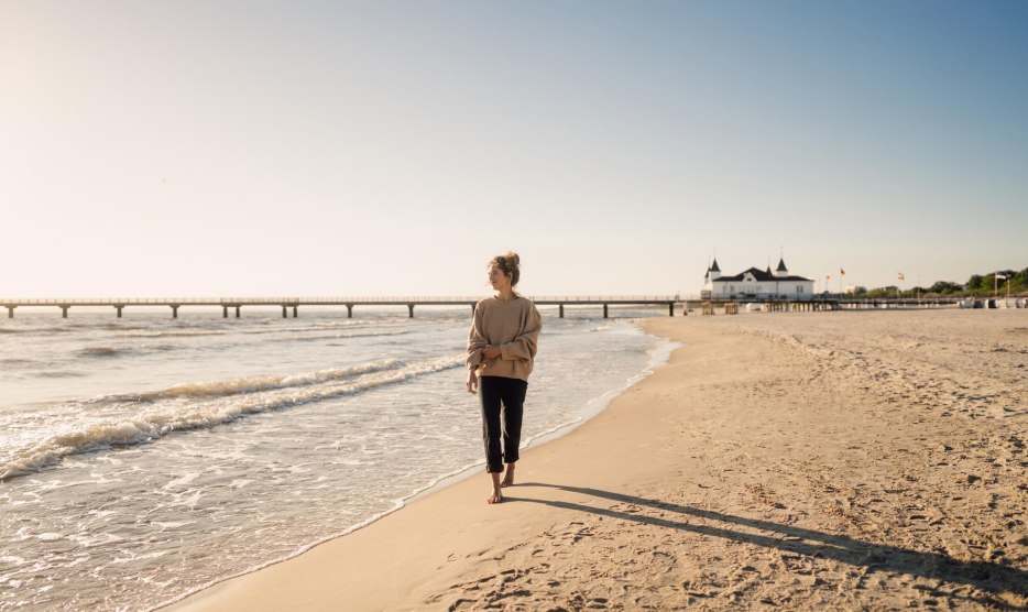 Wandelende vrouw op het strand van Ahlbeck bij zonsopgang met pier op de achtergrond