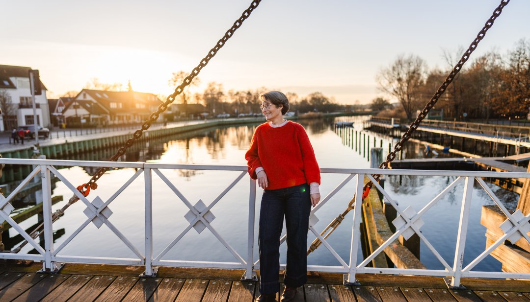 Vrouw op de witte Wiecker basculebrug bij zonsondergang, met de Ryck in Greifswald weerspiegeld op de achtergrond.