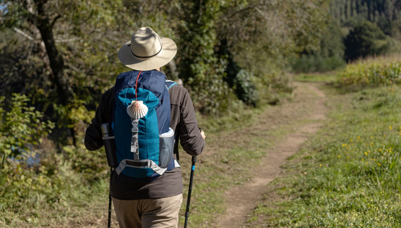 Gezicht van achteren op een pelgrim die over een landelijke weg naar Santiago de Compostela loopt. Camino de Santiago, Camino de Santiago, &copy; AdobeStock