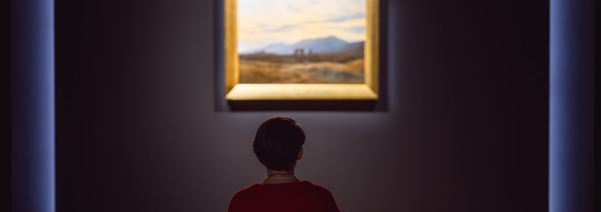 Siła ciszy rozwija się w Galerii Romantyzmu w Pomorskim Muzeum Państwowym w Greifswaldzie. Przed obrazami z epoki romantyzmu otwiera się przestrzeń do kontemplacji i wewnętrznych podróży. Każde dzieło opowiada o tęsknocie, naturze i poszukiwaniu wzniosłości., © MV-T/Gross Zwiedzający siedzi przed romantycznym obrazem pejzażowym w galerii Państwowego Muzeum Pomorskiego.