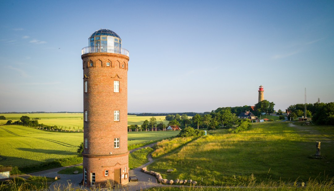 Rode bakstenen Schinkel toren en vuurtoren bij Kaap Arkona op het eiland Rügen, omgeven door groene weiden en velden, met uitzicht op de Baltische Zee op de achtergrond. // De Schinkel toren en de vuurtoren bij Kaap Arkona op het eiland Rügen - een schilderachtige plek met historische charme en een prachtig uitzicht over de Oostzee. // © MV-T/Lueck Rode bakstenen Schinkel toren en vuurtoren bij Kaap Arkona op het eiland Rügen, omgeven door groene weiden en velden, met uitzicht op de Baltische Zee op de achtergrond.
