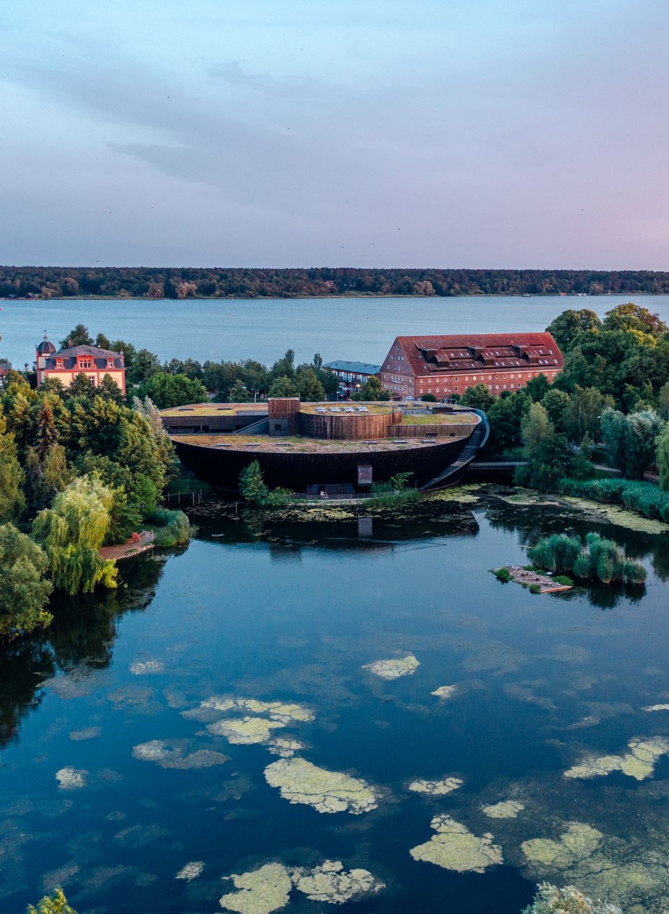 Luchtfoto van het M&uuml;ritzeum in Waren (M&uuml;ritz), omgeven door water en groene natuur bij schemering.