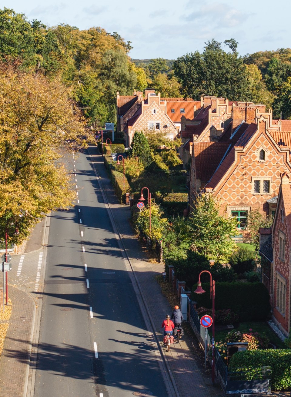 Luchtfoto van een herfstachtige straat in Raben Steinfeld, omzoomd met bomen en historische huizen, met fietsers op de voorgrond.