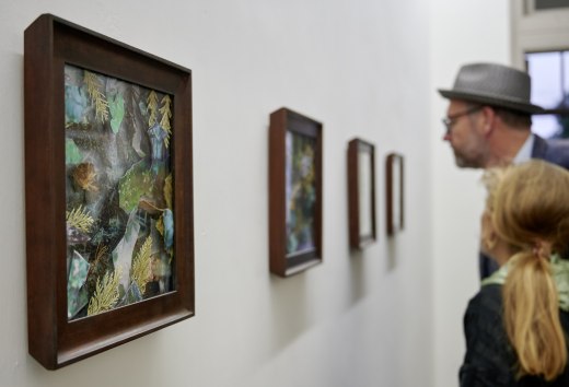 Odwiedzający oglądają oprawione kolaże przyrodnicze na jasnej wystawie podczas serii wydarzeń KUNST HEUTE.