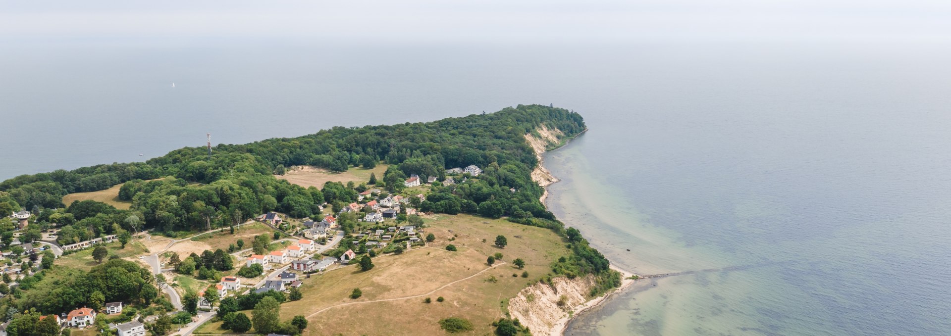 Luchtfoto van de Baltische badplaats Göhren op het eiland Rügen met weidse weiden, een steile kust en de Baltische Zee op de achtergrond onder een licht bewolkte hemel.