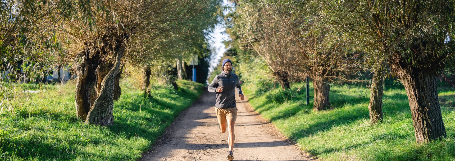  A man jogs along a tree-lined path on the island of Poel, surrounded by green countryside and sunny weather.