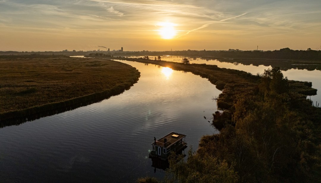 Houseboat on the Peene at sunset, surrounded by a tranquil river landscape and golden light on the horizon. // Sunset over the Peene, while a houseboat floats peacefully on the river. The landscape stretches far into the distance, where sky and water meet. // © TMV Houseboat on the Peene at sunset, surrounded by a tranquil river landscape and golden light on the horizon.