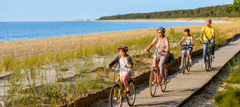 Czteroosobowa rodzina jedzie ścieżką rowerową wzdłuż plaży.