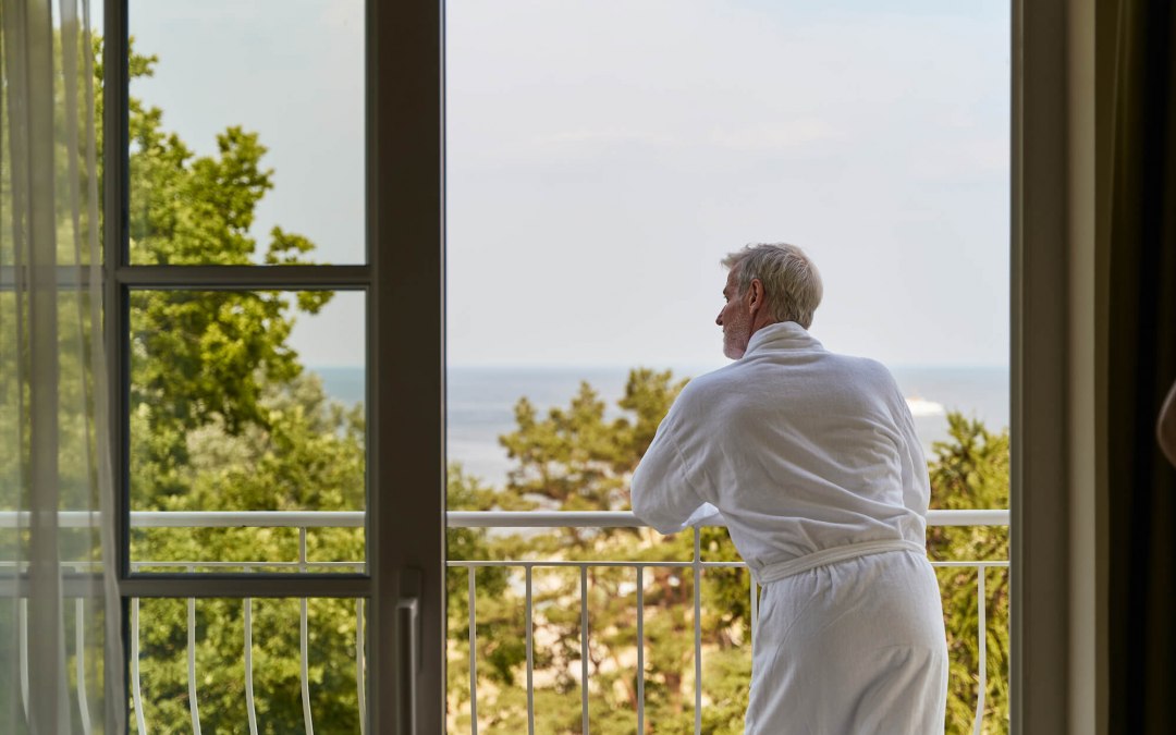 zimmer-mann-im-bademantel-auf-balkon-am-gelaender-strandidyll-heringsdorf, © DSR Hotel Holding