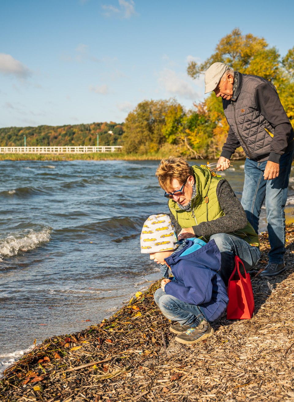 Grandparents sitting with their grandson by the water of Lake Tollensesee in fall