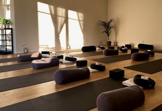 Bright, minimalist yoga room with wooden flooring, several yoga mats, meditation cushions, bolsters and yoga blocks. Warm sunlight shines through large windows and creates a calm, relaxing atmosphere for yoga, meditation and relaxation. // © MOVA PLACE - Yoga & Co. Studio Bright, minimalist yoga room with wooden flooring, several yoga mats, meditation cushions, bolsters and yoga blocks. Warm sunlight shines through large windows and creates a calm, relaxing atmosphere for yoga, meditation and relaxation. // © MOVA PLACE - Yoga & Co. Studio