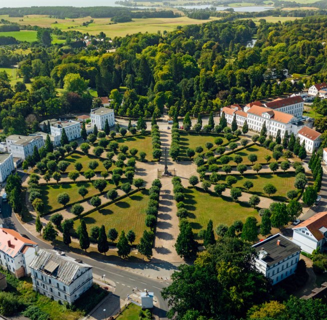 Aerial view of the Circus in Putbus on the island of R&uuml;gen, a circular square with symmetrically arranged trees and classicist buildings, surrounded by green nature and a rural landscape.
