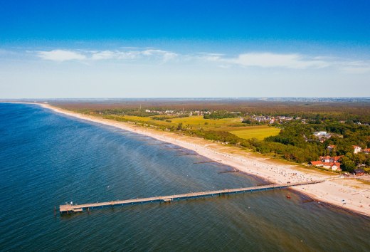 Widok z lotu ptaka na wybrzeże Bałtyku w Graal-Müritz z molo, piaszczystą plażą i nadmorskim lasem. // Molo wystaje do turkusowo-niebieskiej wody, piaszczysta plaża ciągnie się kilometrami wzdłuż wybrzeża. Graal-Müritz zaprasza do pływania, spacerów i wzięcia głębokiego oddechu - między Morzem Bałtyckim a zielonymi lasami leży otwarta przestrzeń na wakacyjne chwile. // © MV-T/Friedrich Widok z lotu ptaka na wybrzeże Bałtyku w Graal-Müritz z molo, piaszczystą plażą i nadmorskim lasem.