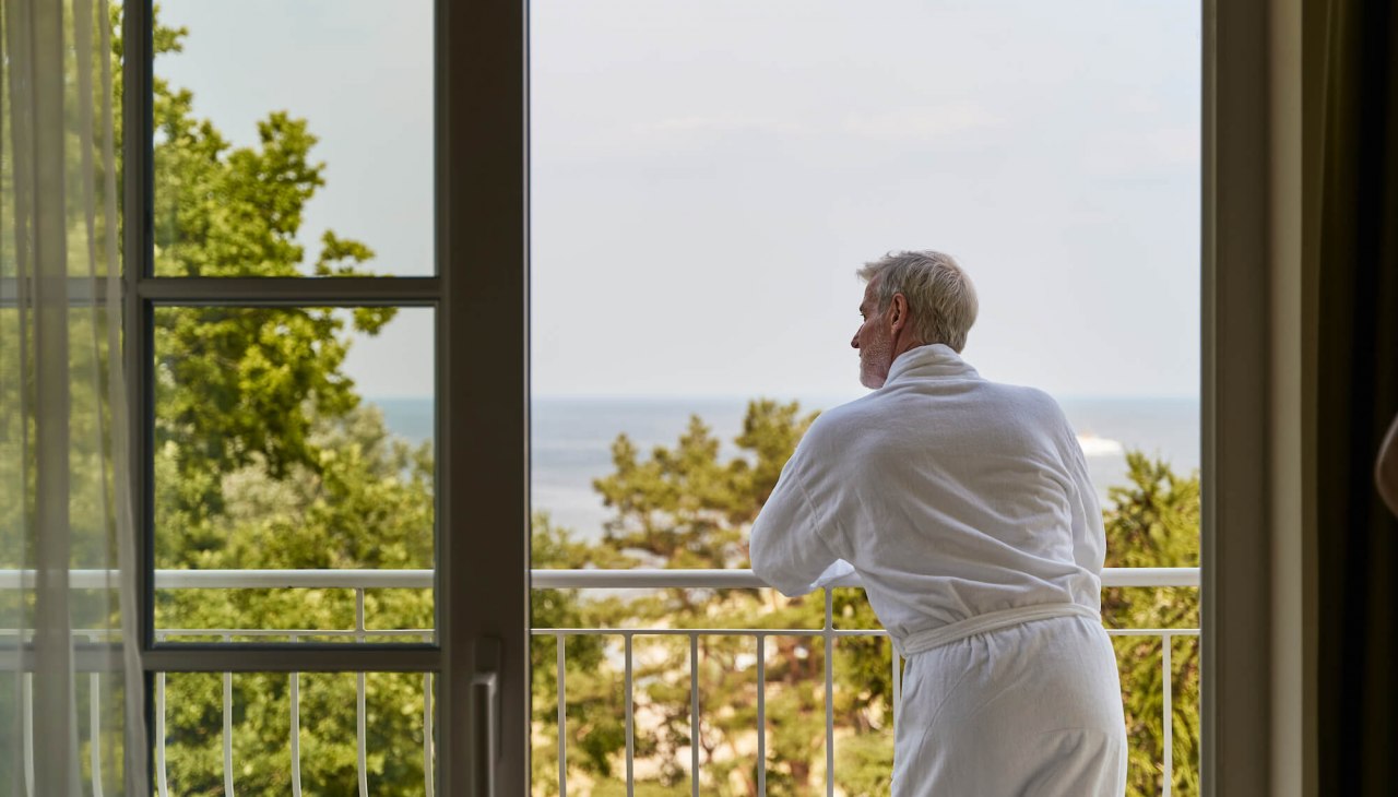 zimmer-mann-im-bademantel-auf-balkon-am-gelaender-strandidyll-heringsdorf, © DSR Hotel Holding