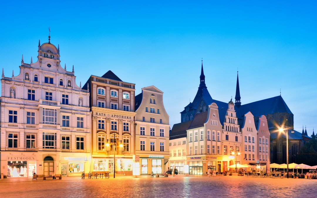 The Neuer Markt in Rostock glows in the evening light: historic facades, church spires and warm windows draw the eye and make you want to take a stroll through Mecklenburg-Vorpommern. // &copy; Francesco Carovillano