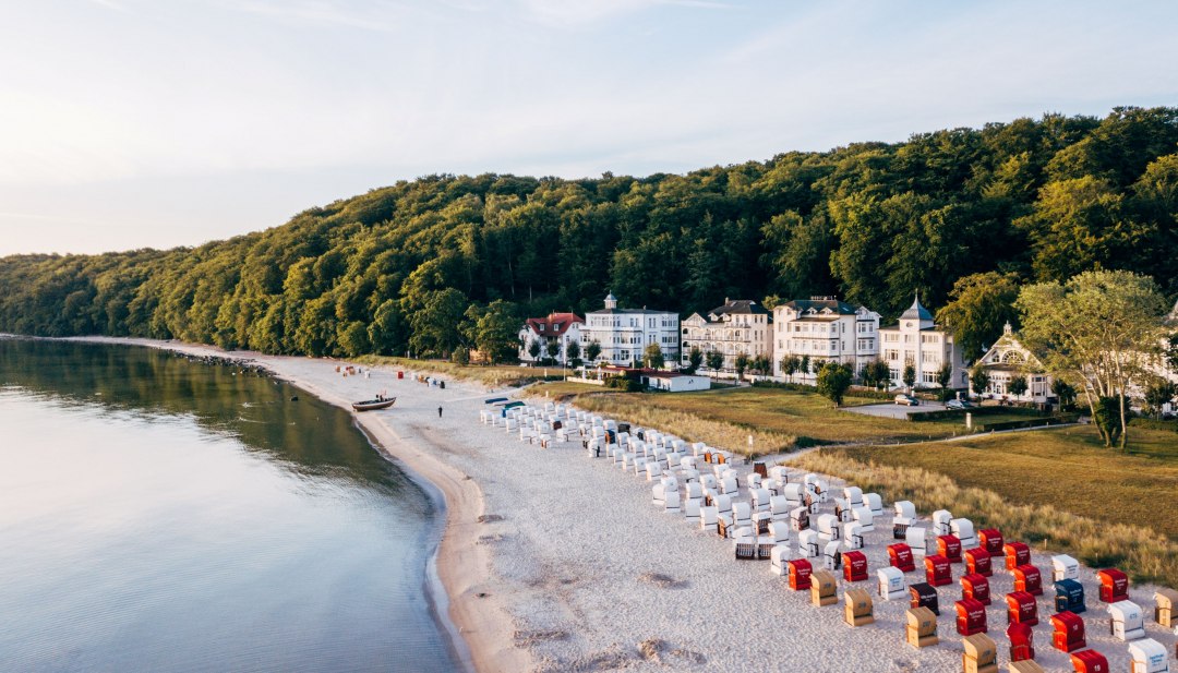 Luchtfoto van het vissersstrand in Binz op Rügen met strandkorven, de rustige Oostzee en villa’s op de boshelling. // Fischerstrand in Binz op Rügen: strandkorven, de rustige Oostzee en badplaatsarchitectuur op de groene kusthelling. // © MV-T/Friedrich Luchtfoto van het vissersstrand in Binz op Rügen met strandkorven, de rustige Oostzee en villa’s op de boshelling.