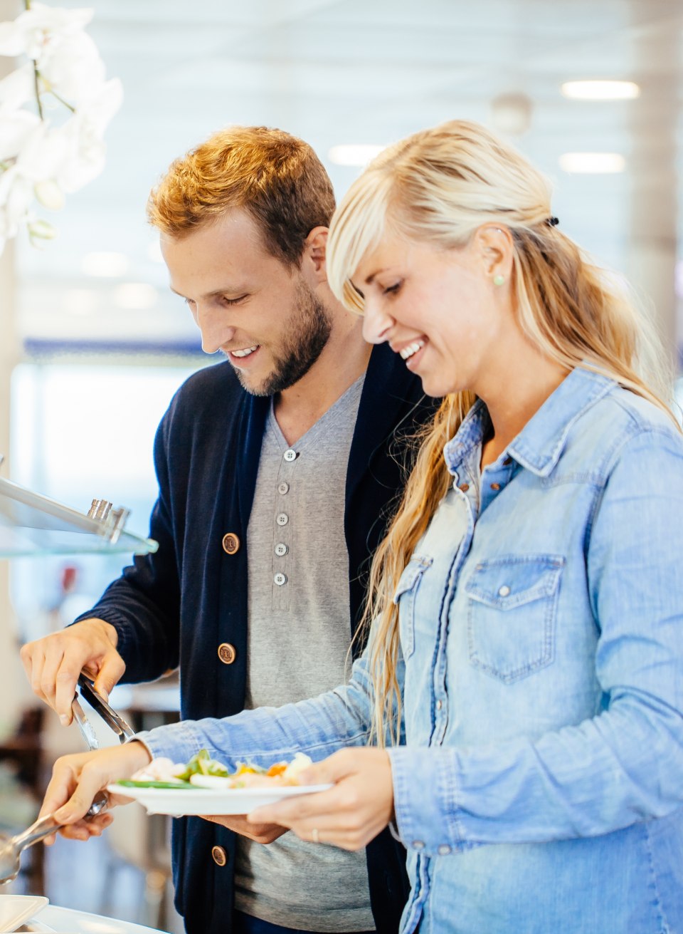 Smiling couple helping themselves to fresh hot food at the buffet on a Scandlines ferry.