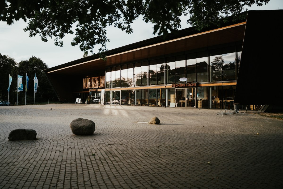 Nowoczesna architektura spotyka się z naturą: Müritzeum w Waren (Müritz) łączy drewno i szkło, tworząc zachęcający zespół. Za fasadą znajduje się największe w Niemczech akwarium dla rodzimych ryb słodkowodnych. Głazy na dziedzińcu przypominają epokę lodowcową - miejsce, które ożywia wiedzę. // © 1000seen.de Nowoczesna architektura spotyka się z naturą: Müritzeum w Waren (Müritz) łączy drewno i szkło, tworząc zachęcający zespół. Za fasadą znajduje się największe w Niemczech akwarium dla rodzimych ryb słodkowodnych. Głazy na dziedzińcu przypominają epokę lodowcową - miejsce, które ożywia wiedzę. // © 1000seen.de