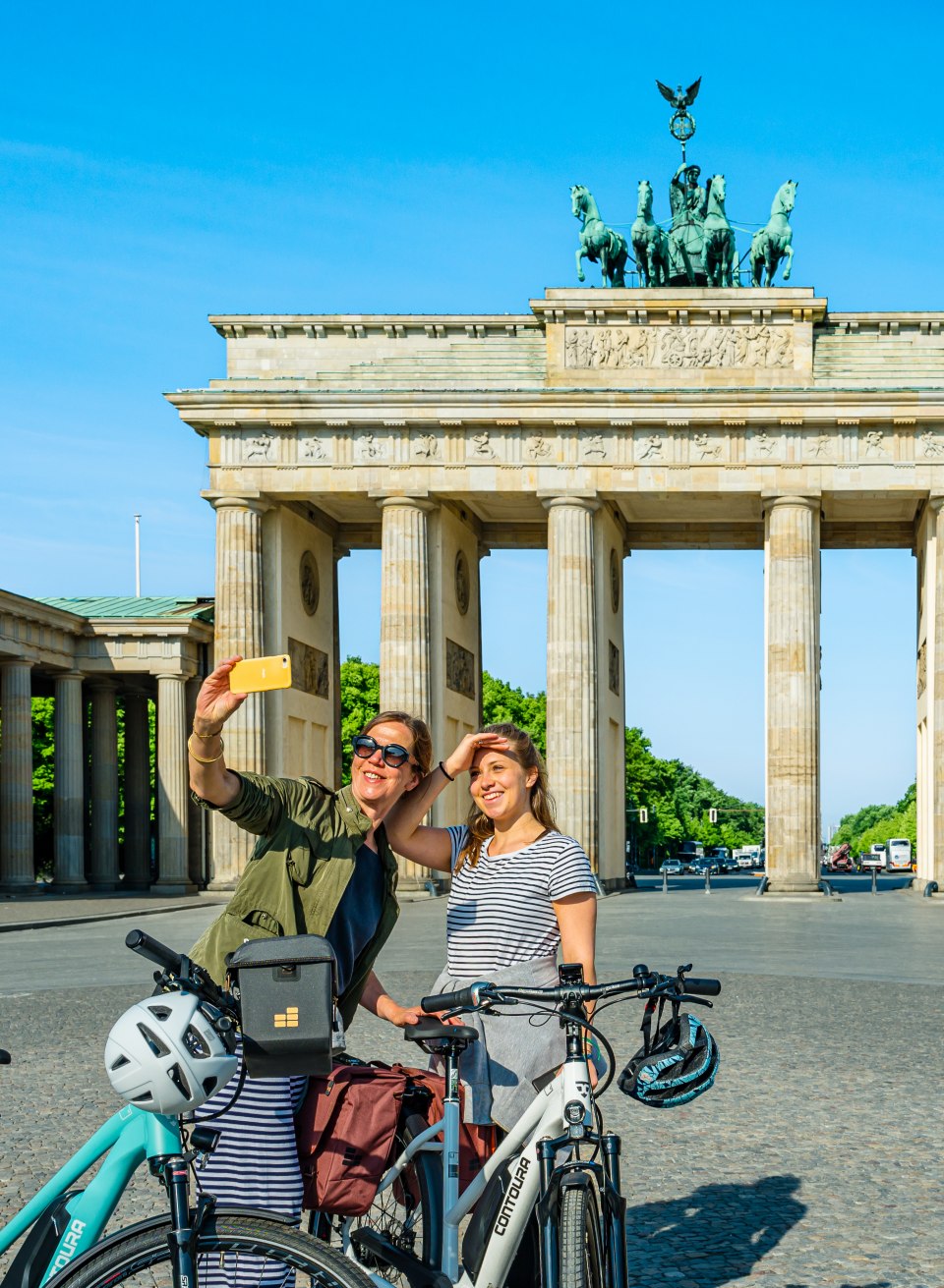 Mother and daughter with bicycles take a selfie in front of the Brandenburg Gate
