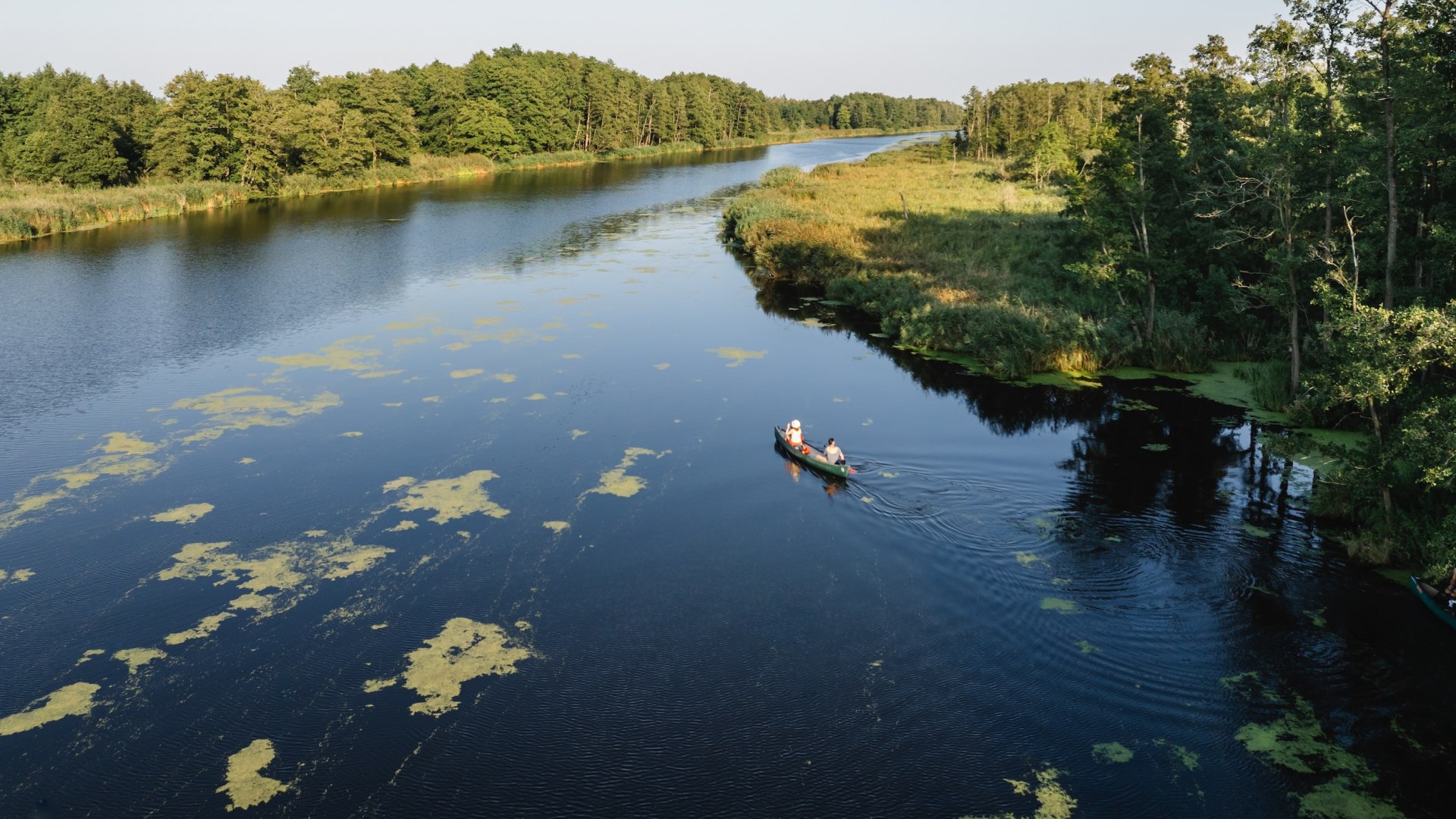 Aerial view of a canoe with two people on the Peene, flanked by a green river landscape. // Pure nature from a bird's eye view - canoe tour on the Peene in Germany's lake district. // © MV-T/Gross Aerial view of a canoe with two people on the Peene, flanked by a green river landscape.