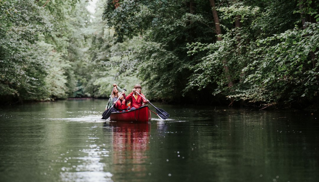 Twee mensen peddelen in een rode kano door een met bomen omzoomde rivier in het Müritz National Park.