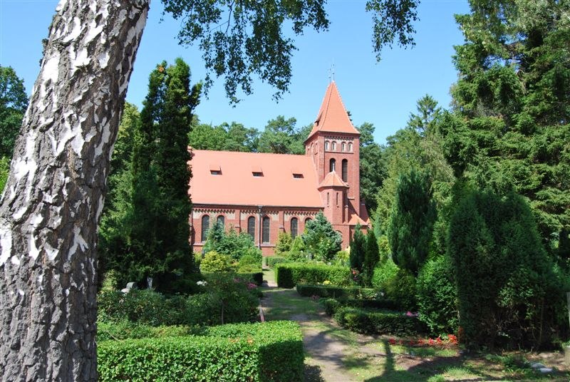 St Luke's Church in Graal-Müritz, een kerk van rode baksteen met een toren, omgeven door groene tuinen en hoge bomen.